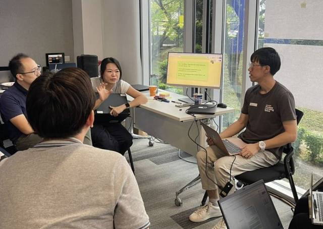 Lance in a small-group discussion, seated with a laptop while another participant shares an idea.